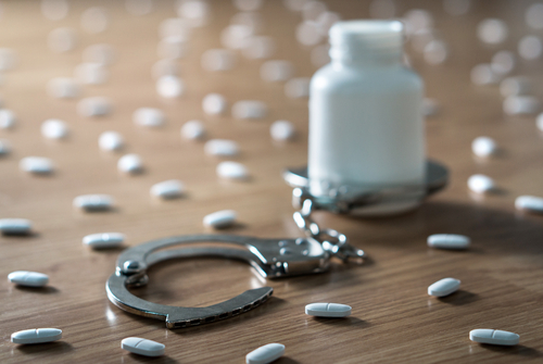 pills scattered on floor with bottle in handcuffs