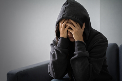 young woman with a hoodie on and her head in her hands