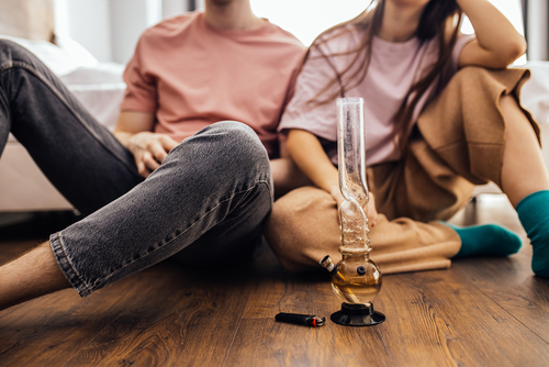 two people sitting on ground with a bong in front of them