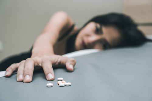 woman reaching for pills laying on bed